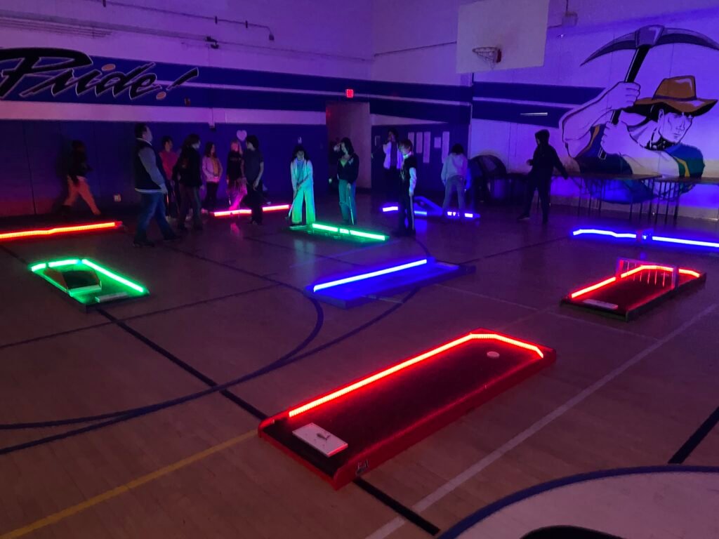 mini golf courses laid out in the dark inside a school gymnasium